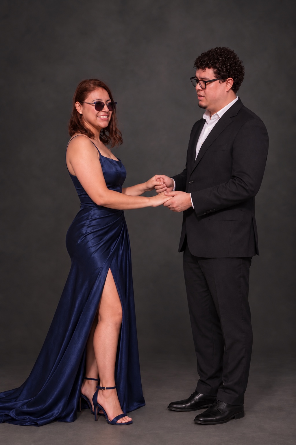 Retrato de pareja tomada de las manos en estudio, ella con vestido azul marino y él con traje negro